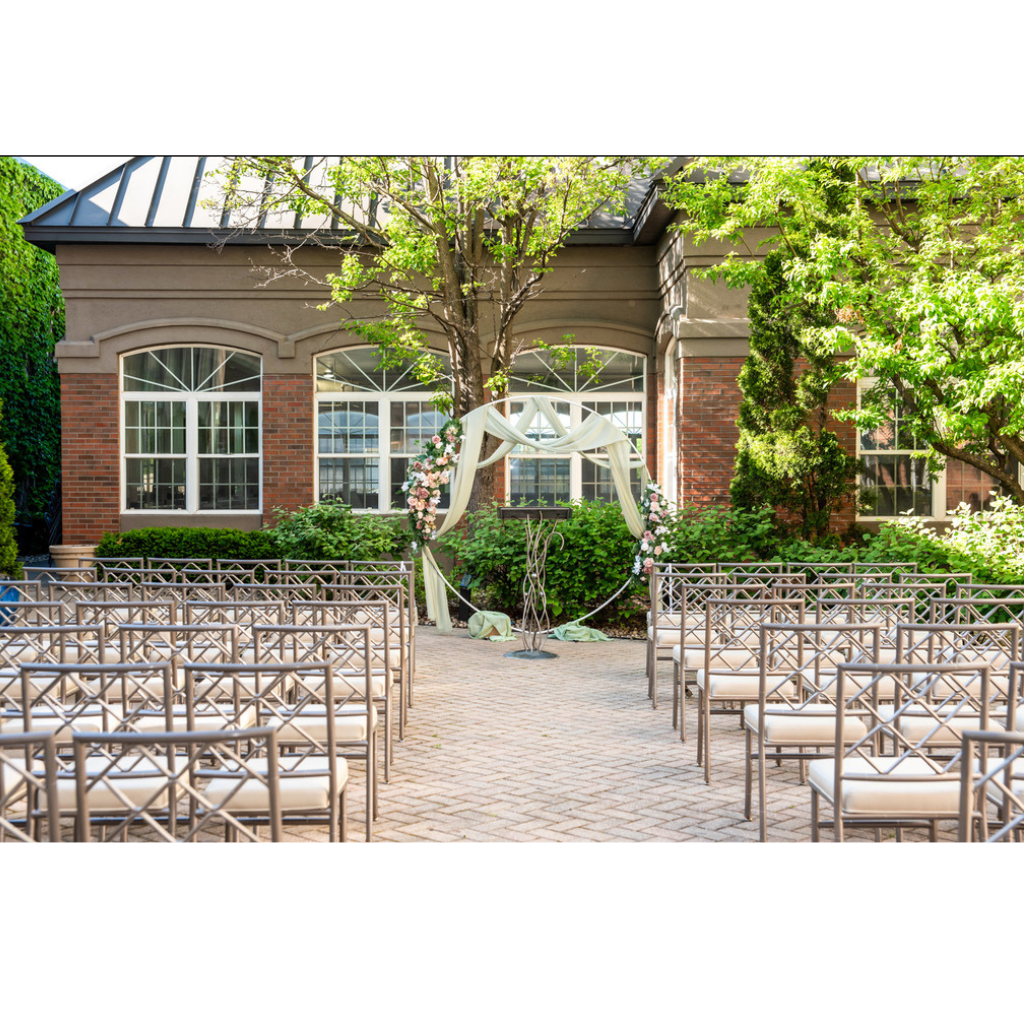 Elegant outdoor wedding ceremony setup with rows of gold chairs facing a white aisle, leading to a decorated altar with white drapery, floral arches